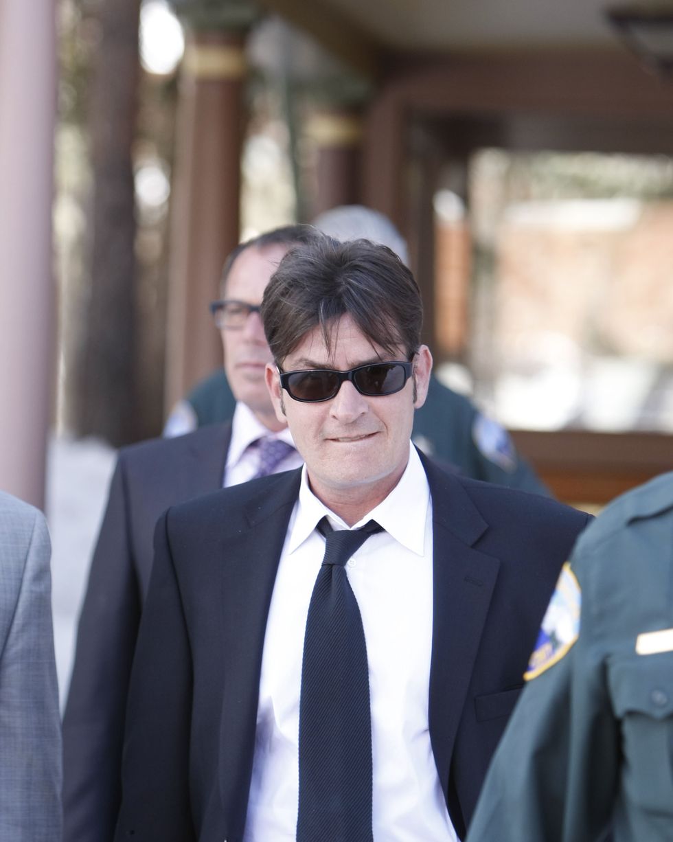 man wearing a suit and sunglasses walking near a building as other people surround him