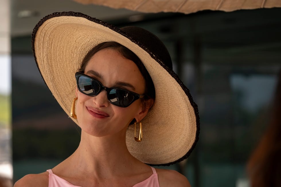a woman wearing a large sun hat and a pink top set against a blurred background