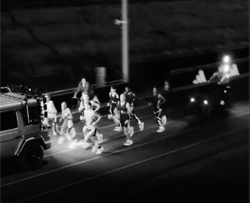 group of runners participating in a nighttime race alongside a vehicle