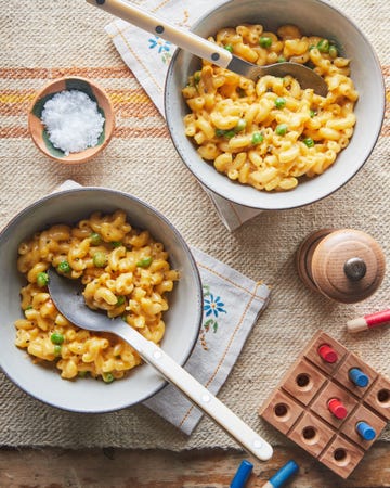 mac 'n cheese with peas in bowls on a table with kids toys