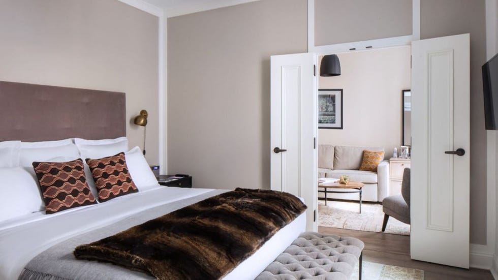 a bedroom with a bed and a view of the living room through the doorway