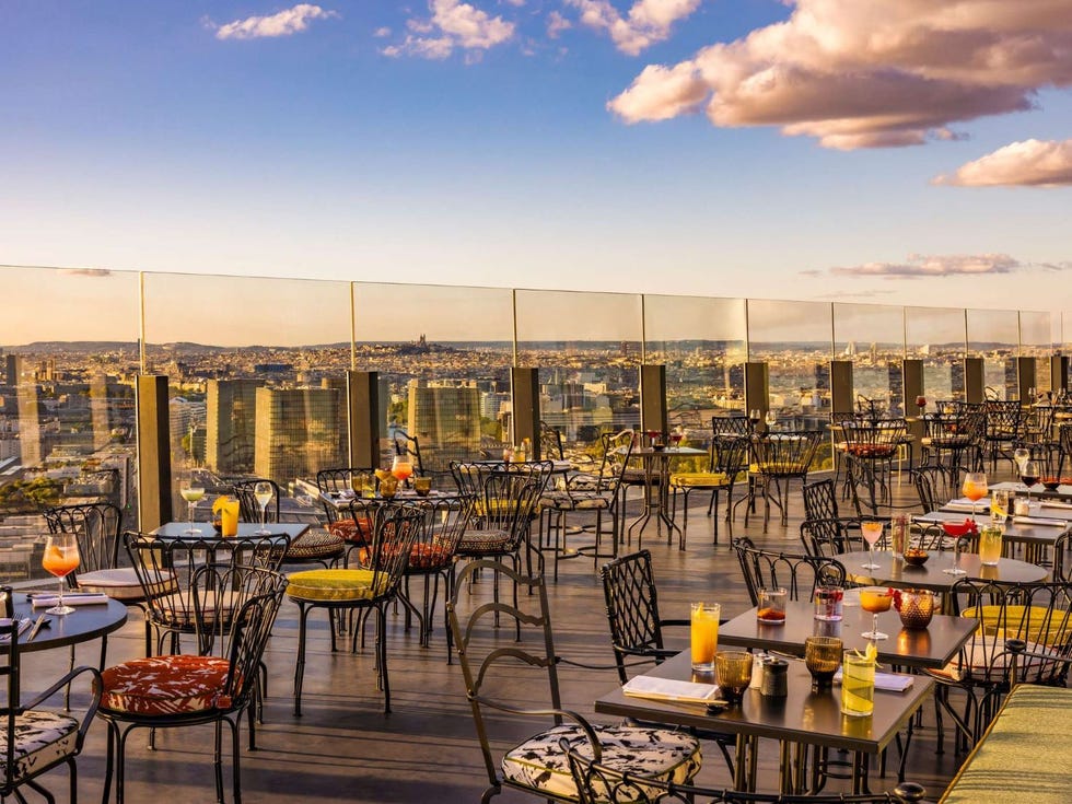 a group of tables and chairs on a deck overlooking a city at too hotel