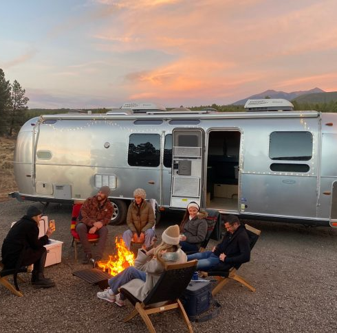 friends sit outside an airstream by a fire in flagstaff, arizona, a good housekeeping pick for best cheap places to travel