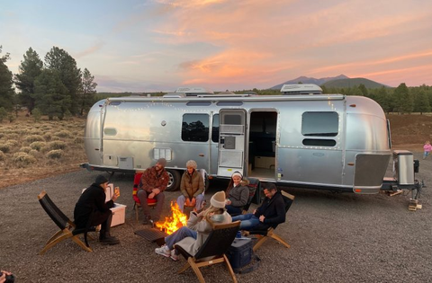 friends sit outside an airstream by a fire in flagstaff, arizona, a good housekeeping pick for best cheap places to travel