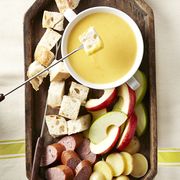 cheddarbeer fondue with bread cubes, sausage, potatoes and apples