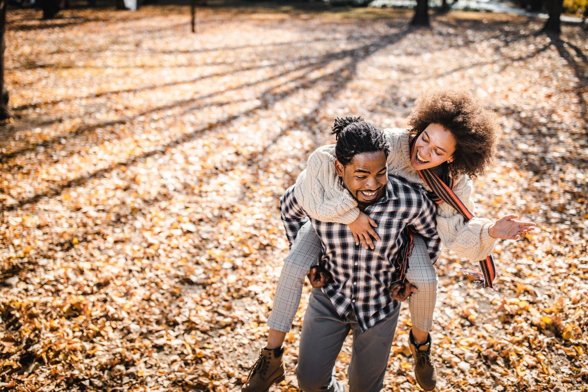 cheerful african american couple piggybacking in autumn at the park