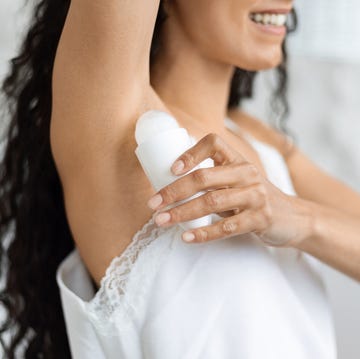 Cheerful arab millennial woman with curly long hair in domestic clothes applying deodorant on armpit cheerful arab millennial woman with curly long hair in domestic clothes applying deodorant on armpit