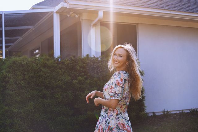 cheerful blonde woman looking over shoulder while walking at the backyard