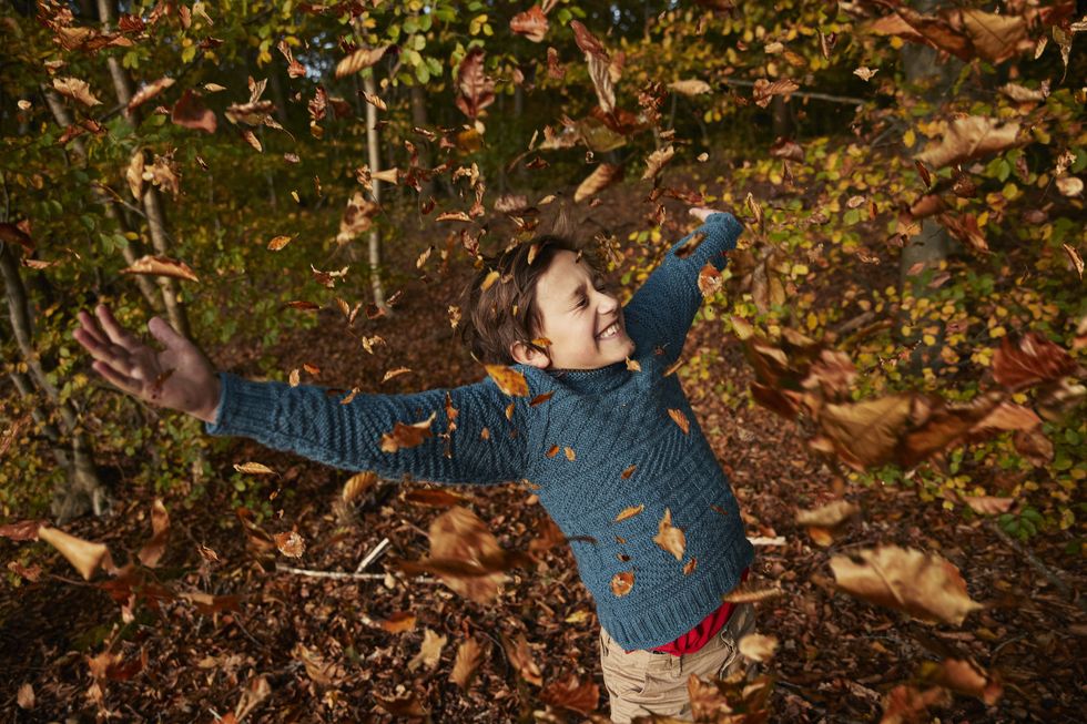 cheerful boy enjoying amidst falling autumn leaves