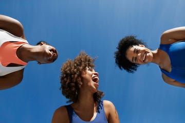 cheerful female athletes in sportswear against blue sky