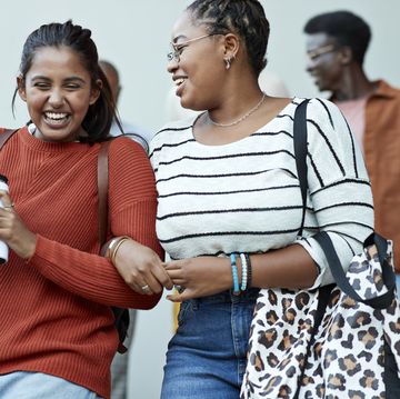 cheerful friends moving down arm in arm at campus