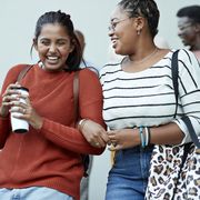cheerful friends moving down arm in arm at campus