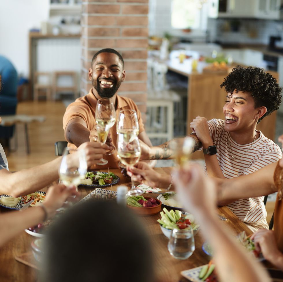 cheerful friends toasting with wine during lunch at home.