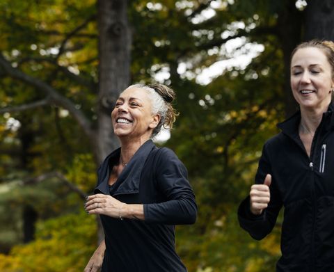 cheerful mature woman with female friend jogging in forest