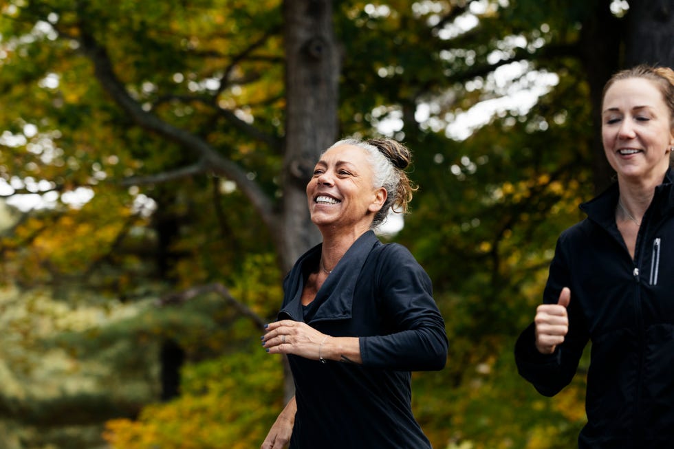 cheerful mature woman with female friend jogging in forest