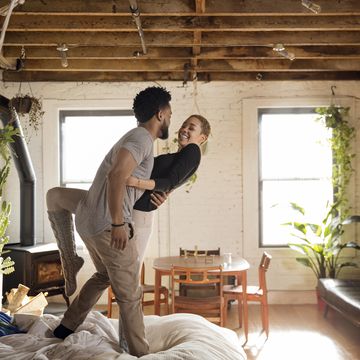 cheerful multiethnic couple dancing on bed at home