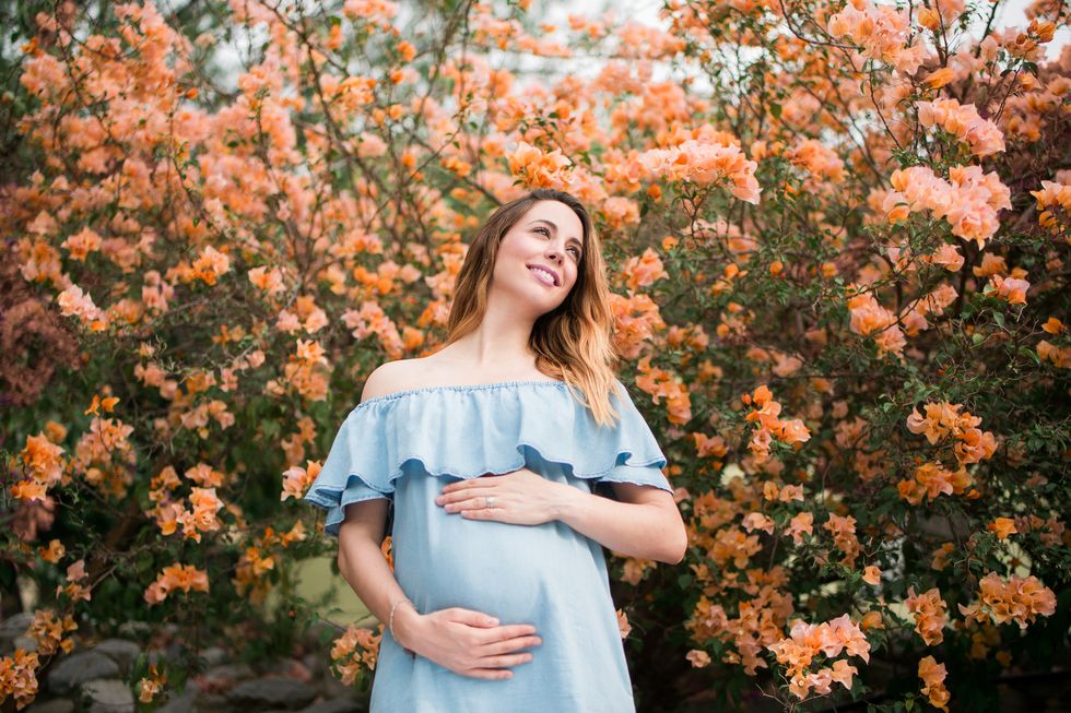 Cheerful pregnant woman standing with flowers in background