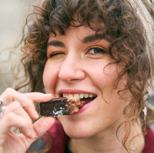 cheerful woman eating candy on street