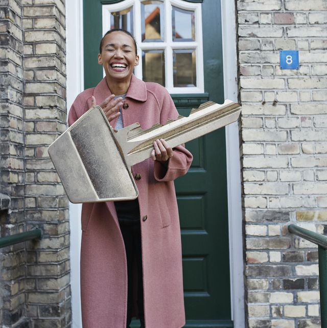 cheerful woman holding large key outside new house