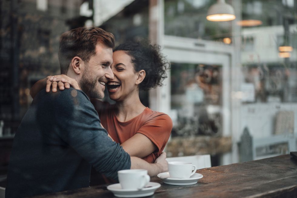 cheerful woman sitting with arm around on man at cafe