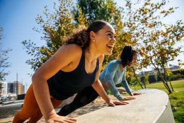 cheerful women doing push ups on retaining wall at park