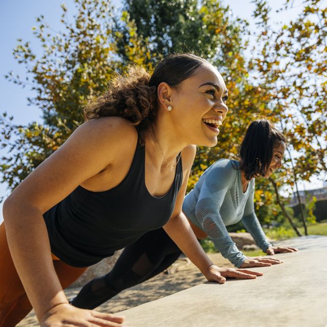 cheerful women doing push ups on retaining wall at park