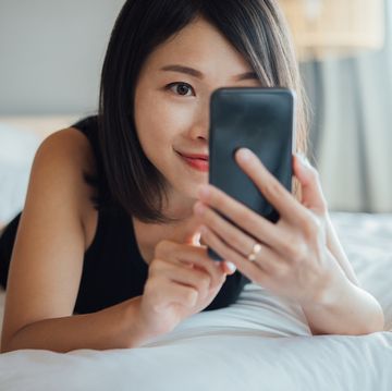 cheerful young beautiful woman using smart phone on bed