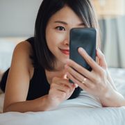 cheerful young beautiful woman using smart phone on bed