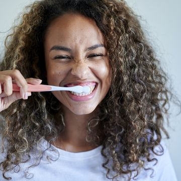 cheerful young woman enjoying while brushing teeth against wall