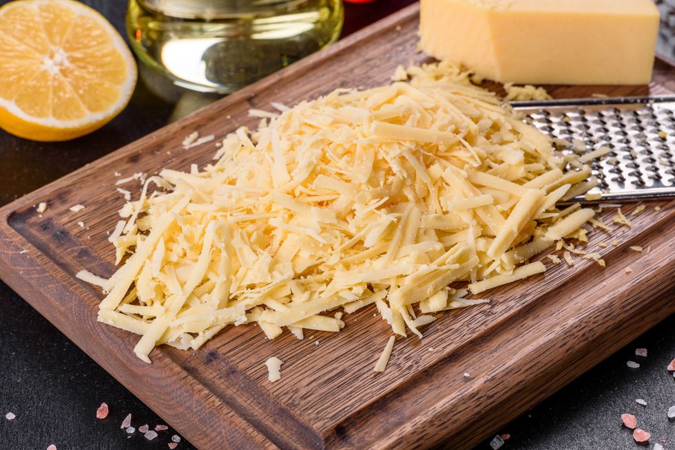 fresh hard cheese grated on a large grater on a wooden cutting board on a dark concrete background
