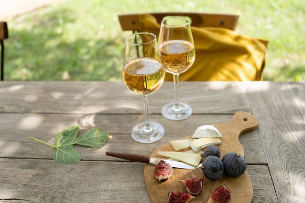 cheese board with figs and white wine on wooden garden table close up