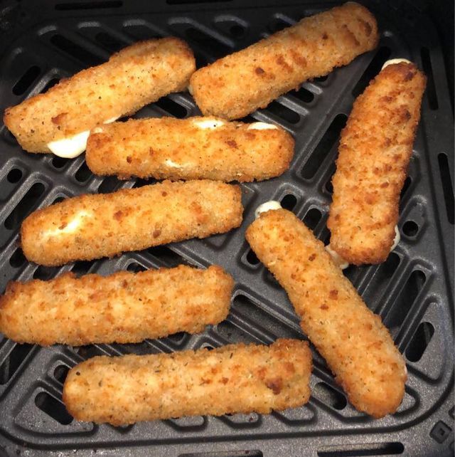 golden mozzarella sticks in an air fryer basket some are split with visible melted cheese