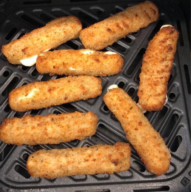 golden mozzarella sticks in an air fryer basket some are split with visible melted cheese