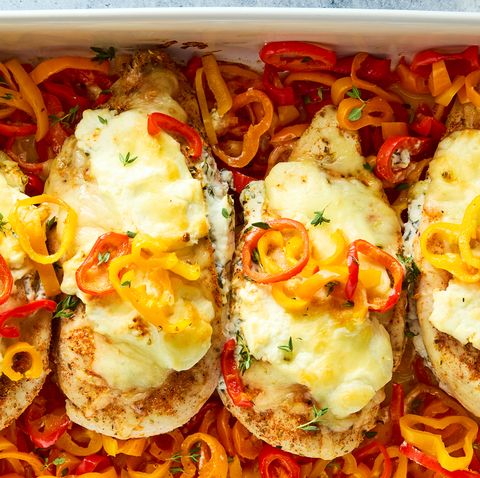 chicken breasts in a casserole dish baked over peppers and topped with cheese