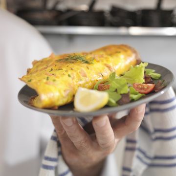 chef holding omelet with scottish smoked salmon, salad and lemon slice in restaurant