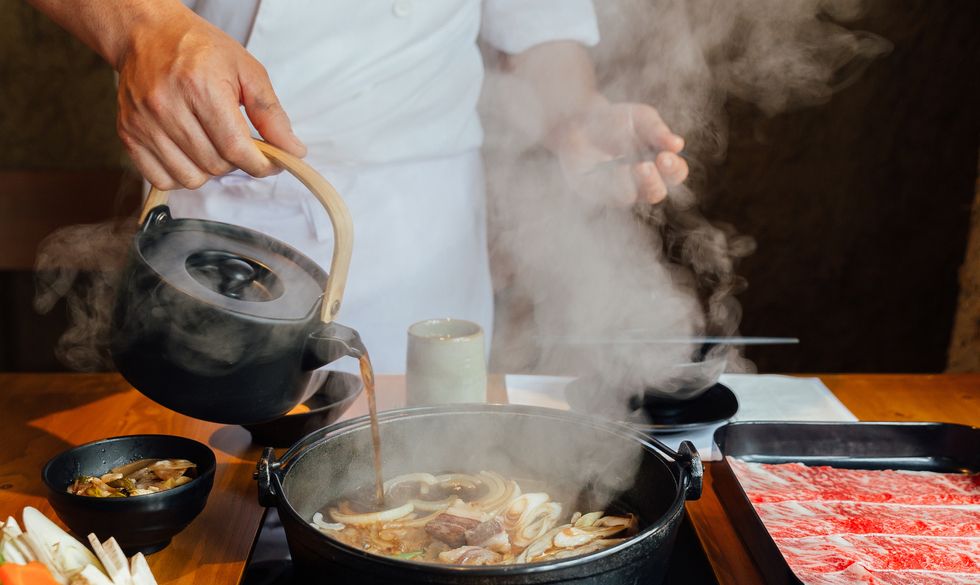 chef is pouring soy sauce on stir fried vegetables such as onion, cabbage, scallion and tofu and more in hot pot with steam before boiling wagyu beef