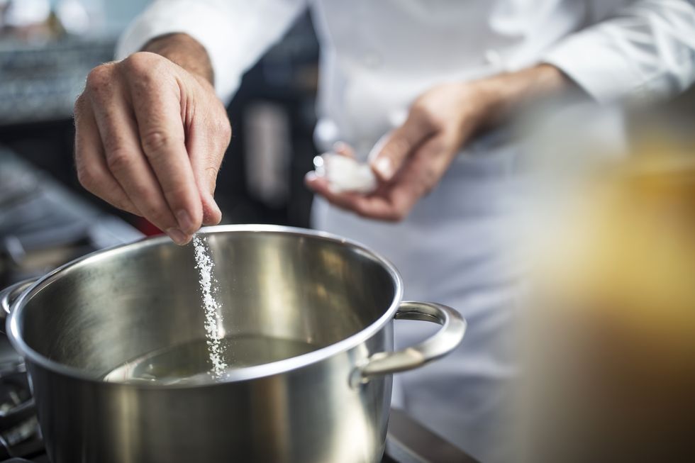 chef putting salt in pan of water on stove, close up