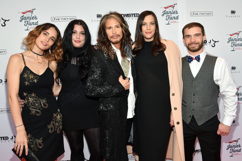 chelsea tyler, mia tyler, steven tyler, liv tyler, and taj tallarico pose for a photo in front of a white backdrop with logos, all are smiling and looking at the camera