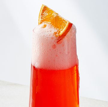 red bubbly drink in a flute garnished with an orange wedge