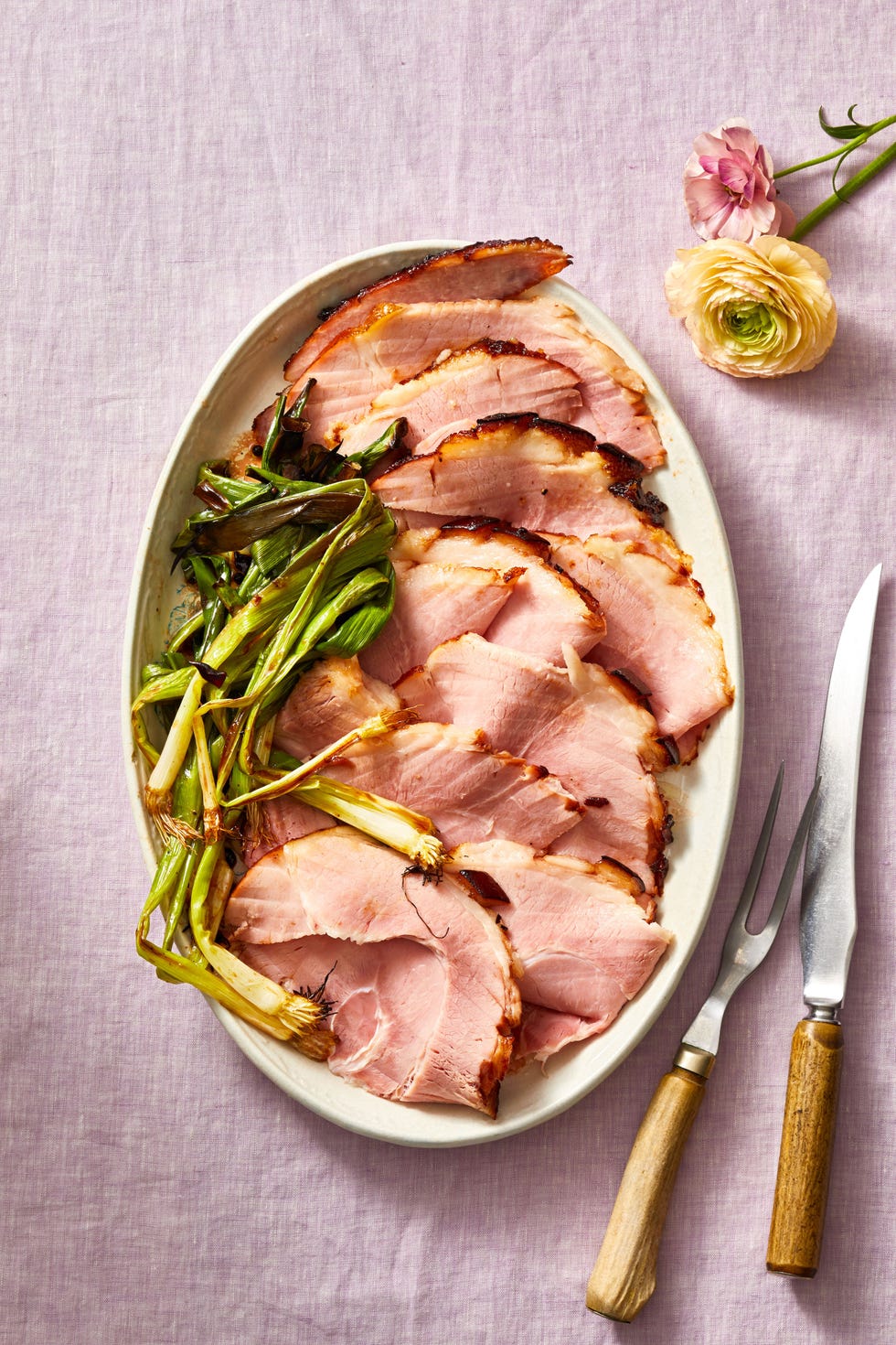 cherry bourbon glazed ham layered on a white plate with a side of grilled scallions