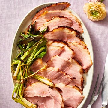 cherry bourbon glazed ham layered on a white plate with a side of grilled scallions