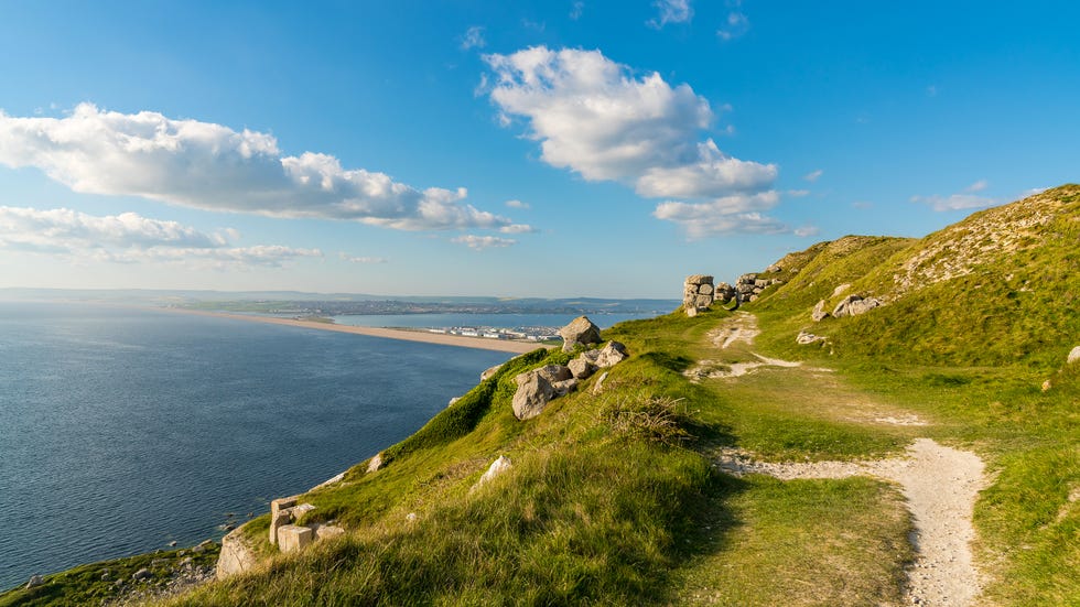 view from the south west coast path towards fortuneswell and chesil beach, isle of portland, jurassic coast, dorset, uk with clouds over weymouth in the background