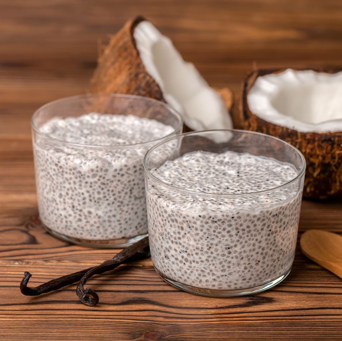 chia pudding in glass, decorated  vanilla pods, spoon and coconuts on wooden background, diet healthy eating and weight loss concept
