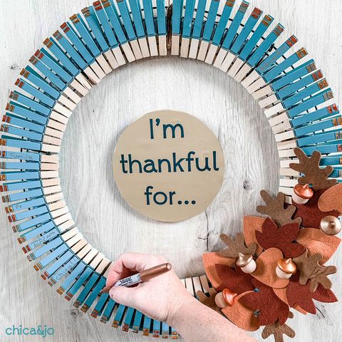 a handwriting something on a teal wreath made of clothespins with felt leaves attached to it