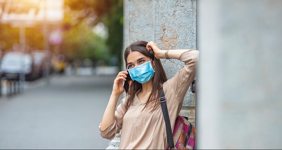 social networking during virus epidemic side view of young woman with face mask walking on the street and talking on the phone young woman with face mask talking on the phone