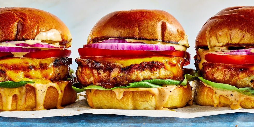 chicken burger topped with sauce, lettuce, sliced red onion, and tomato