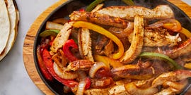 chicken fajitas on a steaming plate with peppers and onions