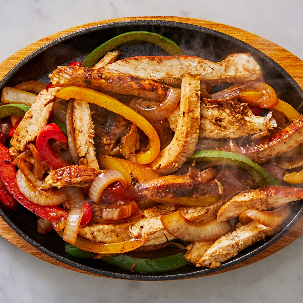 chicken fajitas on a steaming plate with peppers and onions