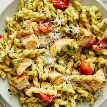 a plate of pasta tossed with pesto with chicken pieces, cherry tomatoes, and parmesan