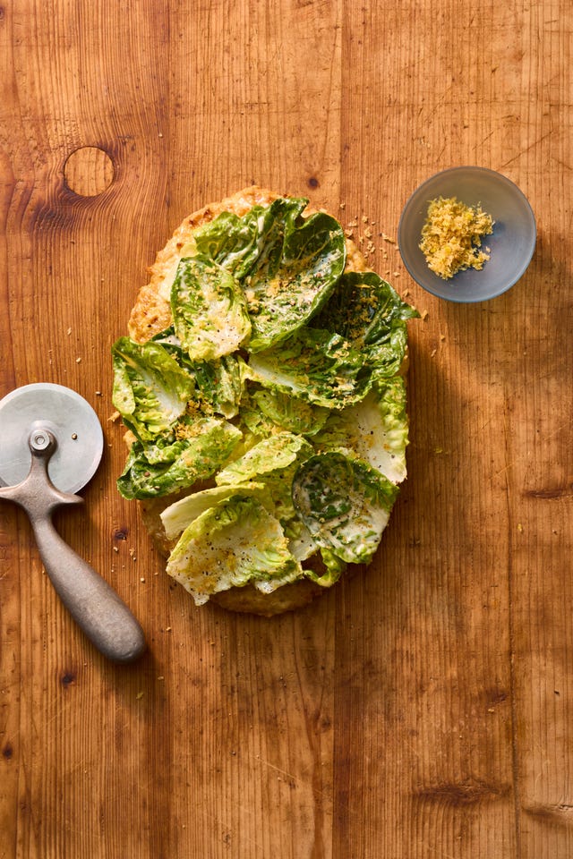 a quote pizza made from ground chicken topped with caesar salad on a wooden board